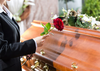 Mourning woman on funeral with red rose standing at casket or coffin
