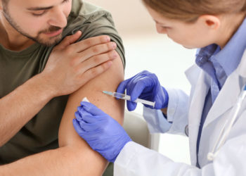 Doctor vaccinating young man in clinic
