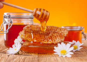 Fresh honey jar with dipper, served on wooden planks